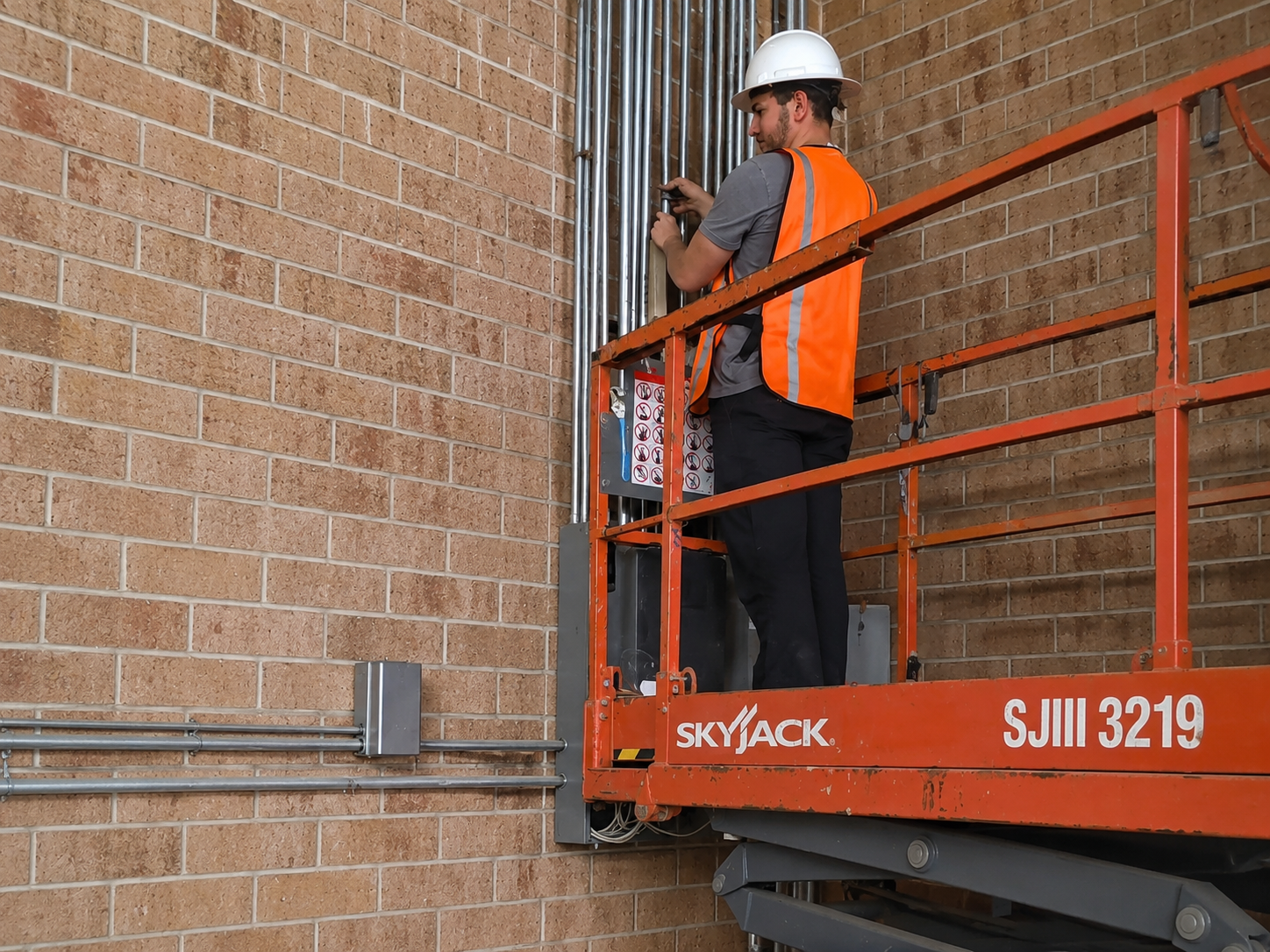 Electrician in hard hat and safety vest on aerial lift installing exterior conduit
